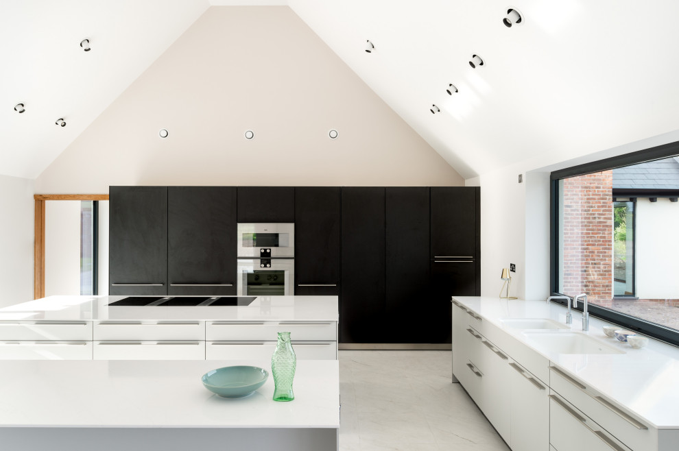 This is an example of a large contemporary l-shaped kitchen in Cheshire with a submerged sink, flat-panel cabinets, composite countertops, integrated appliances, porcelain flooring, multiple islands, window splashback, grey floors and white worktops.