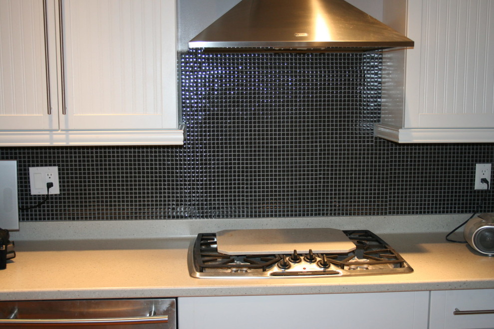 Moderne Küche mit weißen Schränken, Küchenrückwand in Schwarz, Rückwand aus Glasfliesen, Küchengeräten aus Edelstahl und beiger Arbeitsplatte in Calgary