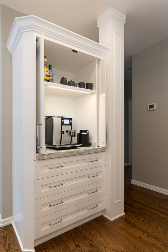 Klassisk inredning av ett stort grå grått kök, med en undermonterad diskho, skåp i shakerstil, vita skåp, bänkskiva i kvarts, grått stänkskydd, stänkskydd i porslinskakel, rostfria vitvaror, mellanmörkt trägolv, en köksö och brunt golv