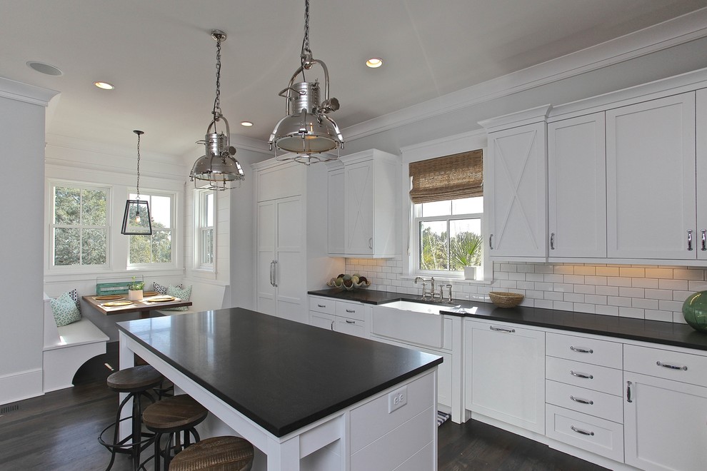 Example of a beach style l-shaped eat-in kitchen design in Charleston with a farmhouse sink, shaker cabinets, white cabinets, granite countertops, white backsplash, subway tile backsplash and paneled appliances