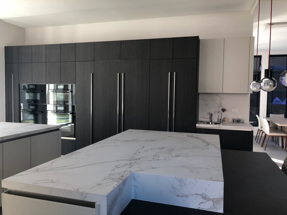 Photo of an expansive contemporary kitchen/diner in Houston with a submerged sink, flat-panel cabinets, dark wood cabinets, engineered stone countertops, white splashback, stone slab splashback, black appliances, ceramic flooring, multiple islands, grey floors and white worktops.