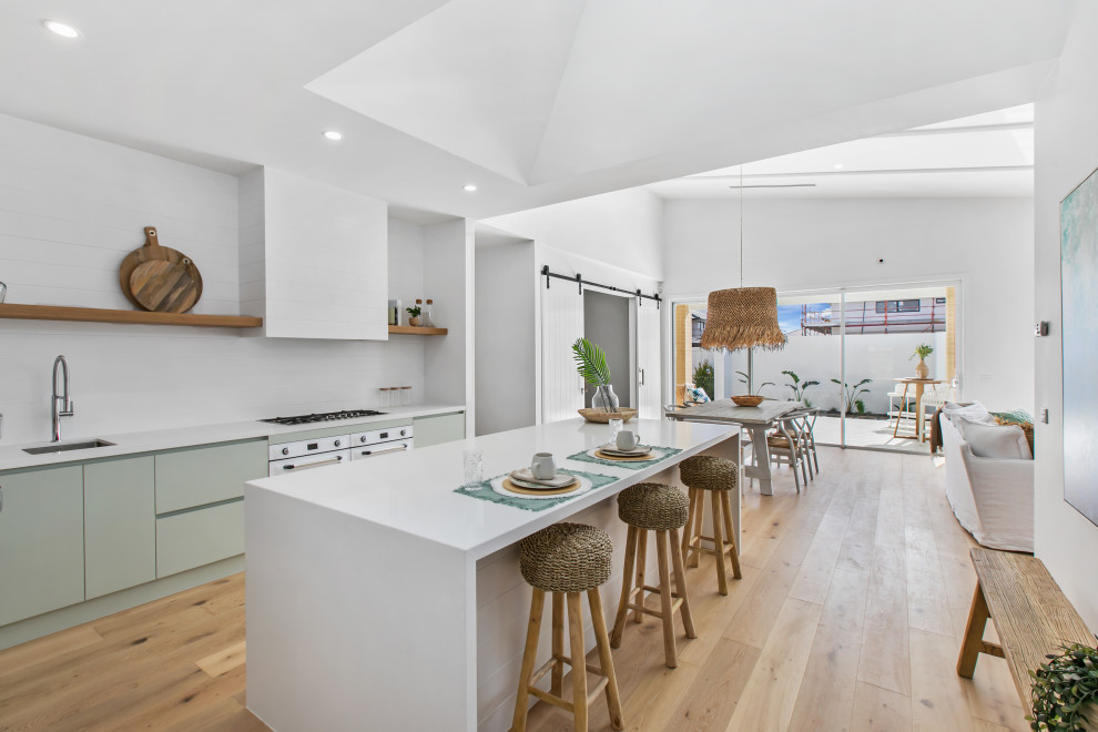 Modern inredning av ett vit linjärt vitt kök och matrum, med en undermonterad diskho, vitt stänkskydd, rostfria vitvaror och en köksö