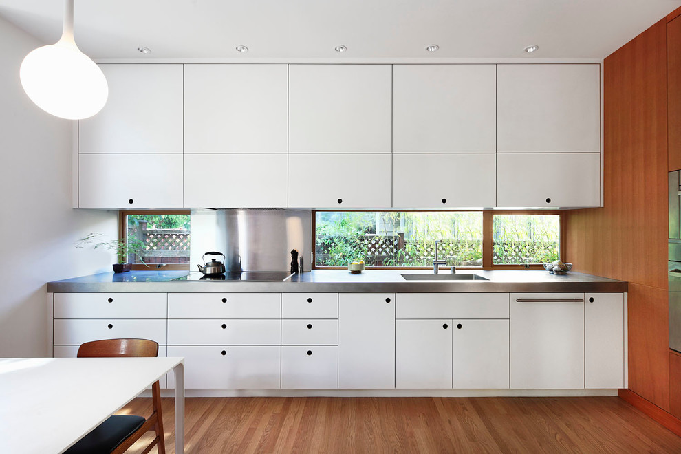 Diseño de cocina actual con armarios con paneles lisos, puertas de armario blancas, electrodomésticos de acero inoxidable y suelo de madera en tonos medios