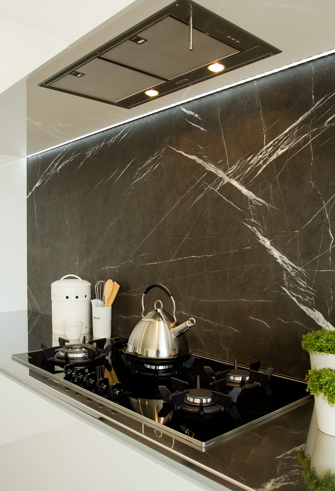 Modern inredning av ett mellanstort svart svart kök, med en enkel diskho, släta luckor, vita skåp, marmorbänkskiva, svart stänkskydd, stänkskydd i sten, rostfria vitvaror, laminatgolv, en köksö och flerfärgat golv