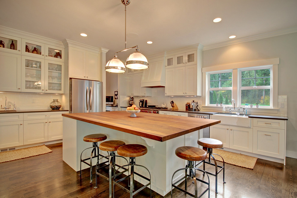 Example of an arts and crafts l-shaped dark wood floor open concept kitchen design in Seattle with a farmhouse sink, shaker cabinets, white cabinets, quartzite countertops, white backsplash, subway tile backsplash, stainless steel appliances and an island