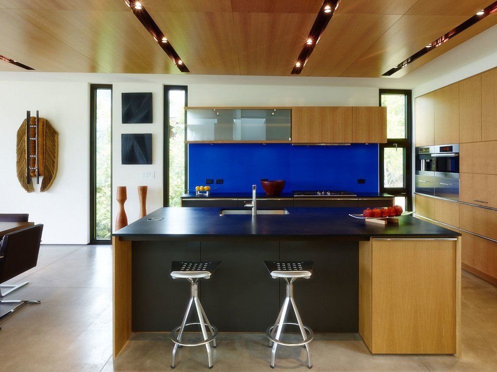Cette image montre une cuisine américaine design en L et bois brun avec un évier encastré, un placard à porte plane, une crédence bleue, un électroménager en acier inoxydable et îlot.