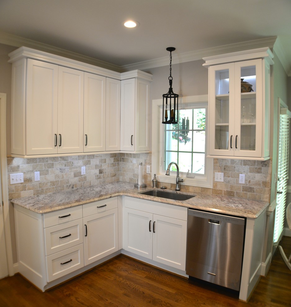 Amerikansk inredning av ett mellanstort kök, med en undermonterad diskho, skåp i shakerstil, vita skåp, granitbänkskiva, brunt stänkskydd, stänkskydd i stenkakel, rostfria vitvaror och mellanmörkt trägolv