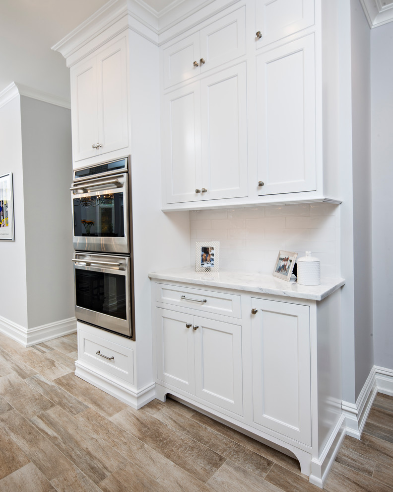 Medium sized traditional l-shaped kitchen/diner in New York with a submerged sink, shaker cabinets, white cabinets, marble worktops, white splashback, metro tiled splashback, stainless steel appliances, light hardwood flooring and an island.