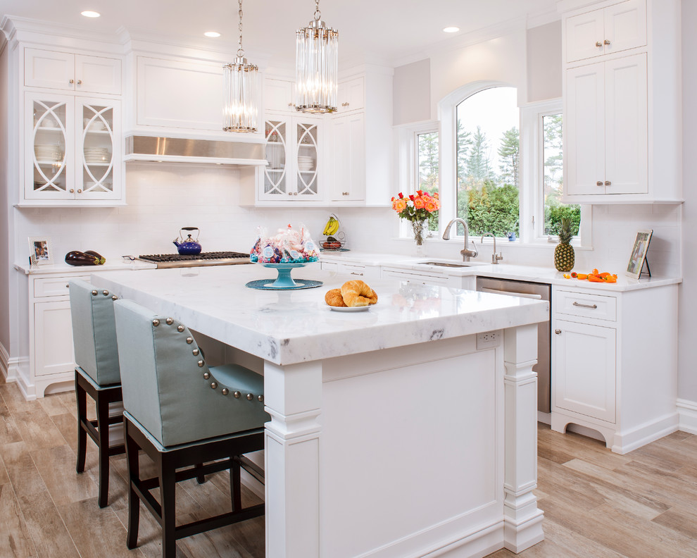 Mid-sized elegant l-shaped light wood floor eat-in kitchen photo in New York with an undermount sink, shaker cabinets, white cabinets, marble countertops, white backsplash, subway tile backsplash, stainless steel appliances, an island and gray countertops