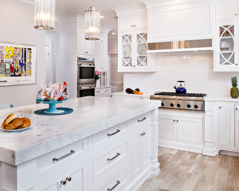 Mid-sized elegant l-shaped light wood floor eat-in kitchen photo in New York with an undermount sink, shaker cabinets, white cabinets, marble countertops, white backsplash, subway tile backsplash, stainless steel appliances and an island