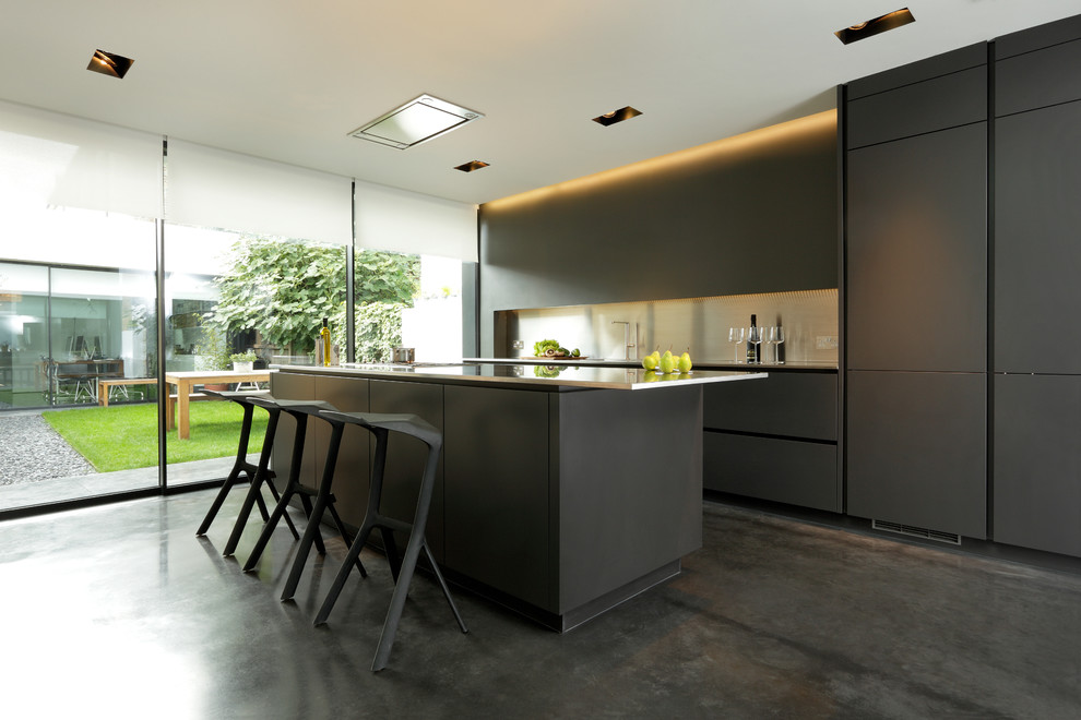 Inspiration för ett mellanstort, avskilt funkis linjärt kök, med en integrerad diskho, släta luckor, svarta skåp, bänkskiva i rostfritt stål, stänkskydd med metallisk yta, svarta vitvaror, betonggolv och en köksö