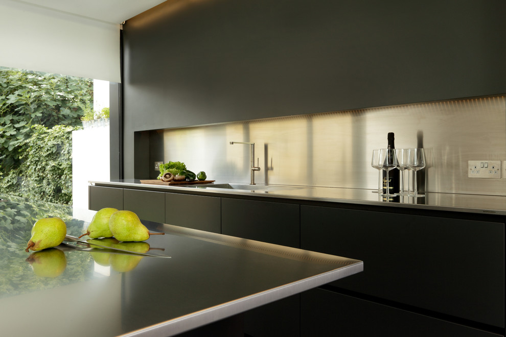 Bild på ett stort, avskilt funkis linjärt kök, med en integrerad diskho, släta luckor, svarta skåp, bänkskiva i rostfritt stål, stänkskydd med metallisk yta, svarta vitvaror, betonggolv och en köksö
