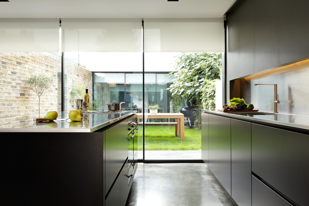 Foto på ett stort, avskilt funkis linjärt kök, med en nedsänkt diskho, släta luckor, svarta skåp, bänkskiva i rostfritt stål, stänkskydd med metallisk yta, integrerade vitvaror och betonggolv