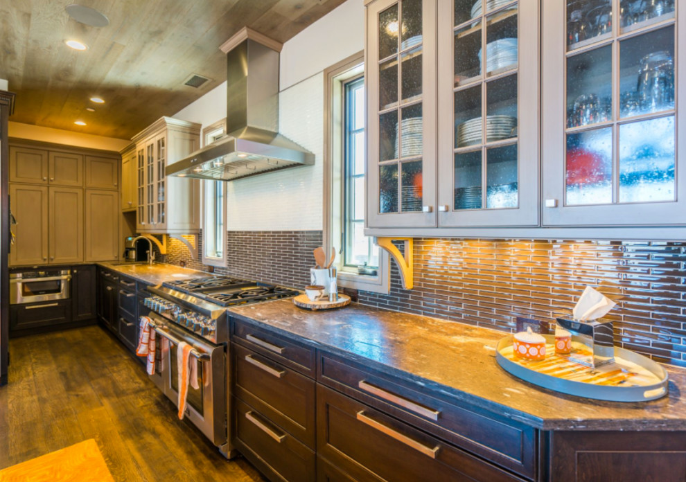 Inredning av ett amerikanskt stort kök, med en undermonterad diskho, luckor med infälld panel, bänkskiva i glas, stänkskydd i stickkakel, rostfria vitvaror, mörkt trägolv, en köksö, brunt golv, skåp i mörkt trä och grått stänkskydd