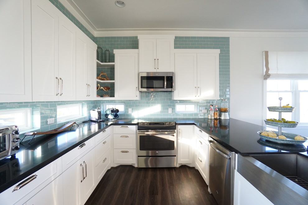 Example of a mid-sized beach style u-shaped vinyl floor open concept kitchen design in Houston with a farmhouse sink, shaker cabinets, white cabinets, quartz countertops, blue backsplash, glass tile backsplash, stainless steel appliances and a peninsula