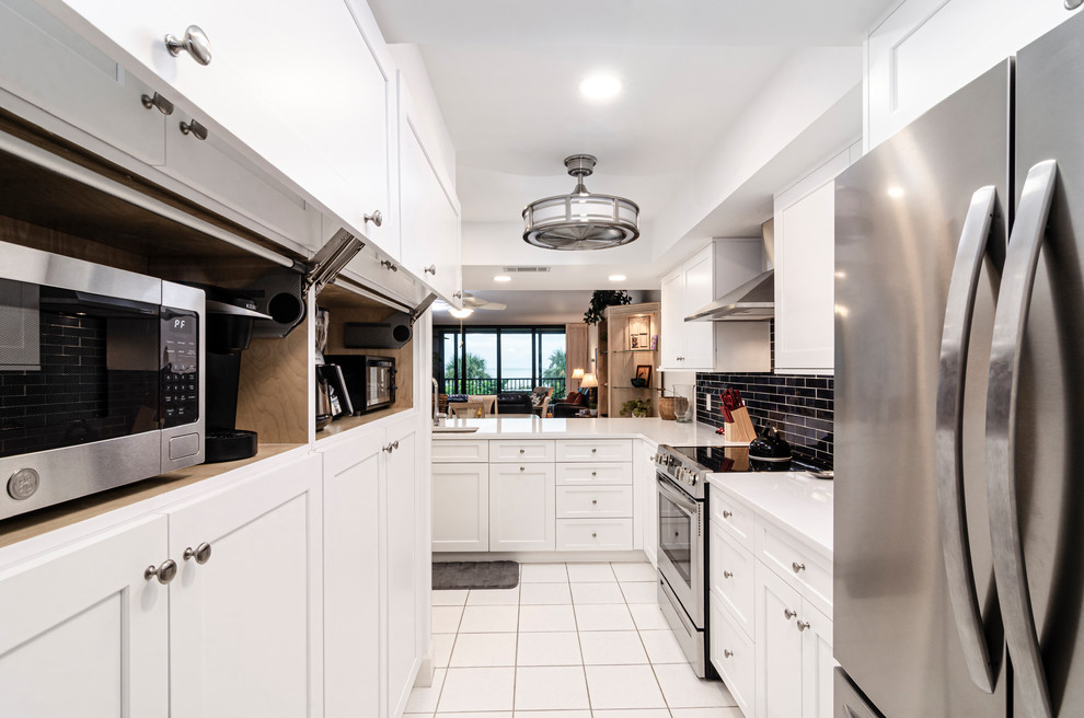 Example of a mid-sized transitional l-shaped porcelain tile and white floor enclosed kitchen design in Miami with an undermount sink, shaker cabinets, white cabinets, quartz countertops, black backsplash, subway tile backsplash, stainless steel appliances, a peninsula and white countertops