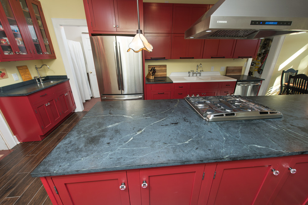 Immagine di una cucina design di medie dimensioni con lavello a doppia vasca, ante con bugna sagomata, ante rosse, top in saponaria, elettrodomestici in acciaio inossidabile, parquet scuro e pavimento marrone