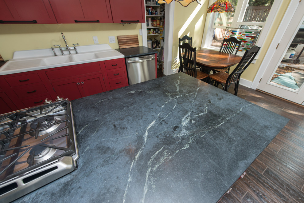 Inredning av ett modernt mellanstort kök, med en dubbel diskho, luckor med upphöjd panel, röda skåp, bänkskiva i täljsten, rostfria vitvaror, mörkt trägolv, en köksö och brunt golv