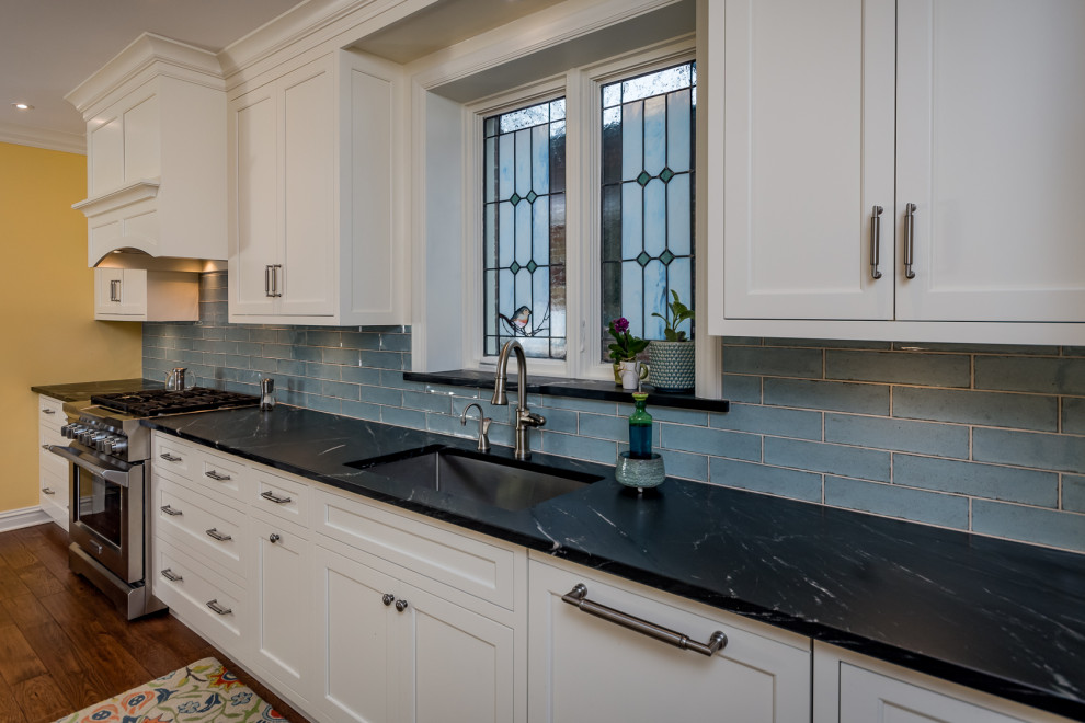 Inspiration for a large transitional galley medium tone wood floor eat-in kitchen remodel in St Louis with an undermount sink, recessed-panel cabinets, white cabinets, soapstone countertops, blue backsplash, subway tile backsplash, stainless steel appliances, an island and black countertops