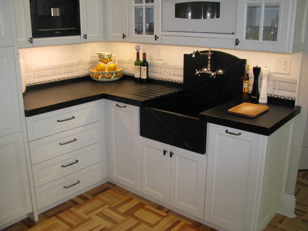 Klassisk inredning av ett avskilt, mellanstort u-kök, med en integrerad diskho, luckor med infälld panel, vita skåp, bänkskiva i täljsten, flerfärgad stänkskydd, stänkskydd i keramik, ljust trägolv och flerfärgat golv