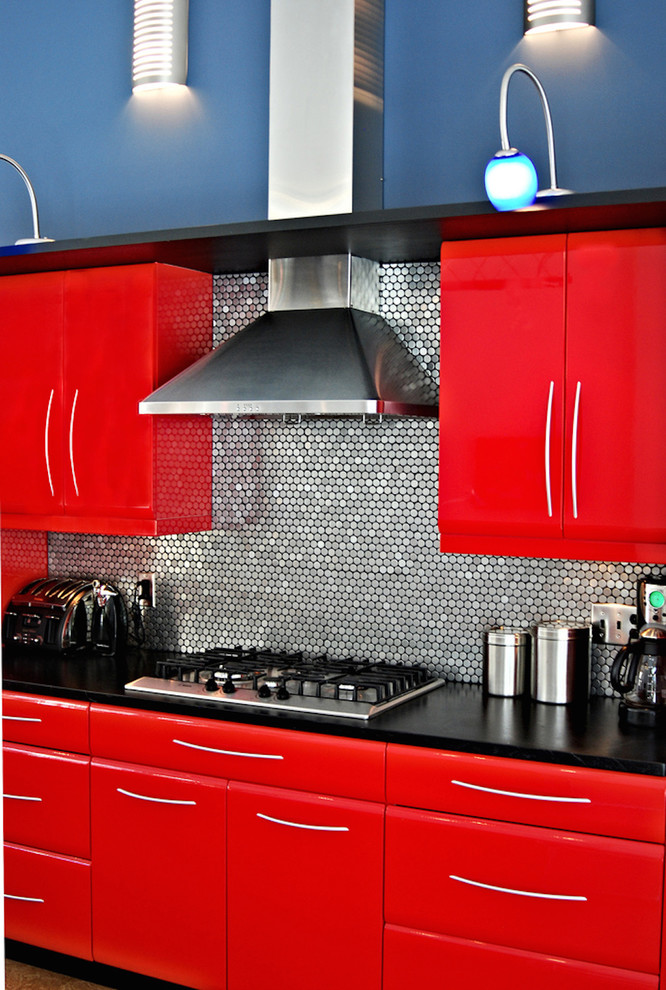 Bild på ett funkis kök, med släta luckor, röda skåp, stänkskydd med metallisk yta och rostfria vitvaror