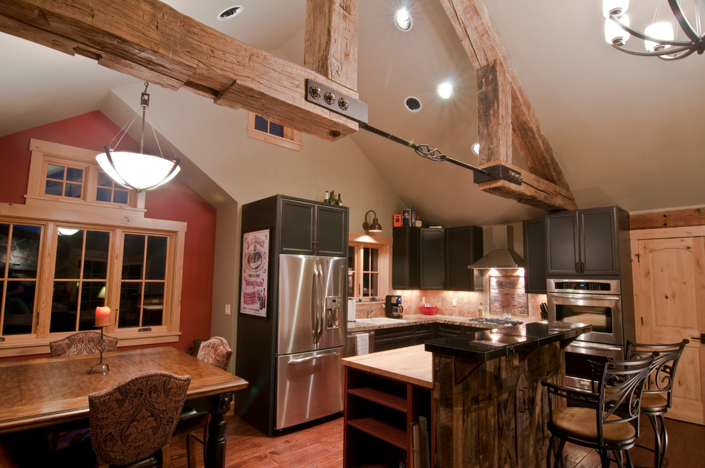 Photo of a medium sized rustic u-shaped open plan kitchen in Denver with a built-in sink, raised-panel cabinets, black cabinets, ceramic splashback, beige splashback, stainless steel appliances and an island.