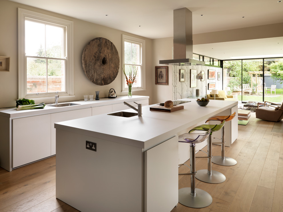 Cette photo montre une cuisine ouverte parallèle tendance avec un placard à porte plane, des portes de placard blanches, un sol en bois brun et îlot.