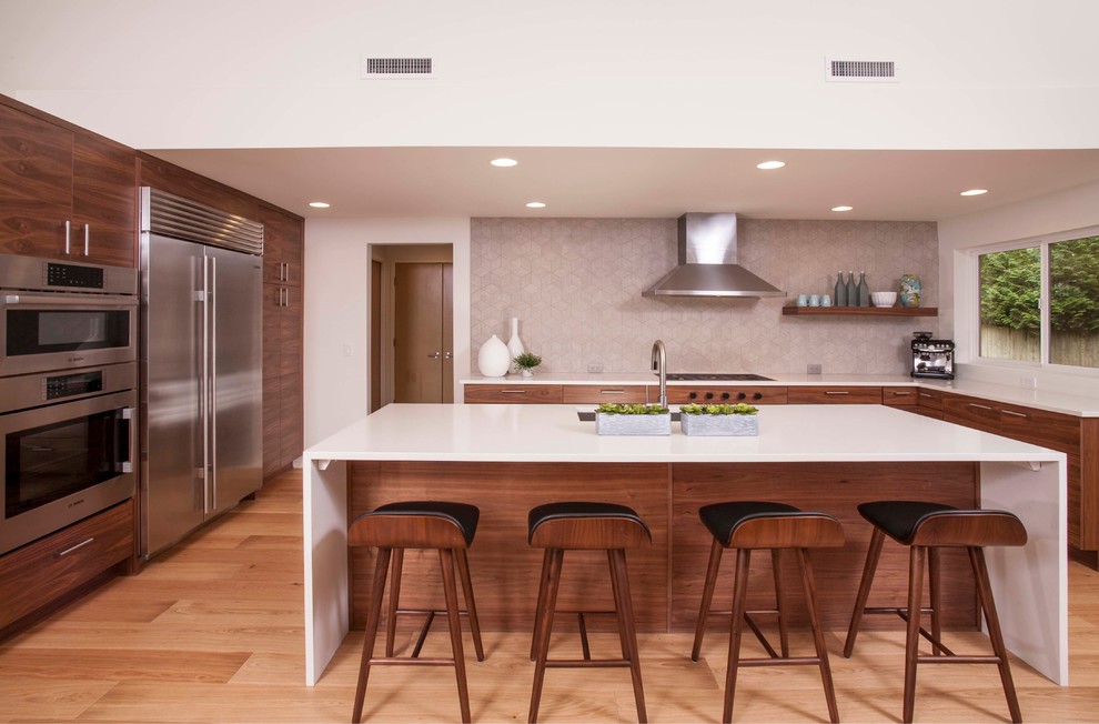 Moderne Küche in U-Form mit flächenbündigen Schrankfronten, Kücheninsel, Unterbauwaschbecken, dunklen Holzschränken, Küchenrückwand in Beige, Küchengeräten aus Edelstahl, hellem Holzboden und weißer Arbeitsplatte in Seattle