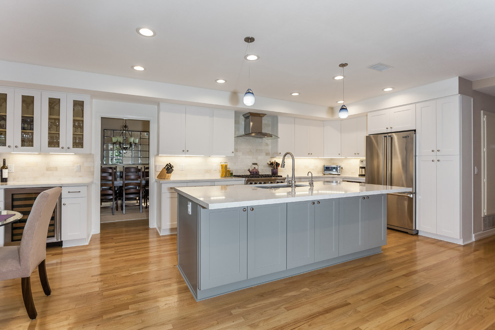 Modern inredning av ett mellanstort vit vitt kök, med en undermonterad diskho, skåp i shakerstil, vita skåp, bänkskiva i kvarts, beige stänkskydd, stänkskydd i stenkakel, rostfria vitvaror, ljust trägolv, en köksö och gult golv
