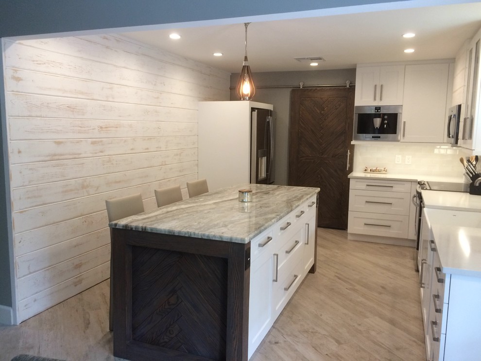 Design ideas for a medium sized shabby-chic style l-shaped kitchen/diner in Tampa with a belfast sink, shaker cabinets, white cabinets, engineered stone countertops, white splashback, metro tiled splashback, stainless steel appliances, porcelain flooring and an island.