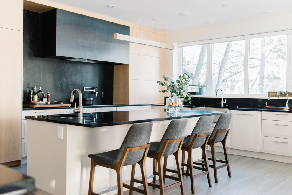 Große Moderne Küche in U-Form mit Landhausspüle, Speckstein-Arbeitsplatte, Küchenrückwand in Schwarz, Kücheninsel, schwarzer Arbeitsplatte, flächenbündigen Schrankfronten, hellen Holzschränken, Elektrogeräten mit Frontblende und weißem Boden in Edmonton