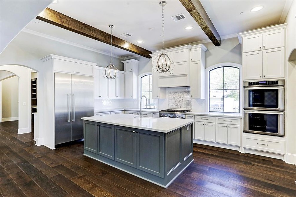 Large contemporary u-shaped open plan kitchen in Houston with a drop-in sink, shaker cabinets, white cabinets, quartzite benchtops, white splashback, stone tile splashback, stainless steel appliances, dark hardwood floors, with island, brown floor and white benchtop.