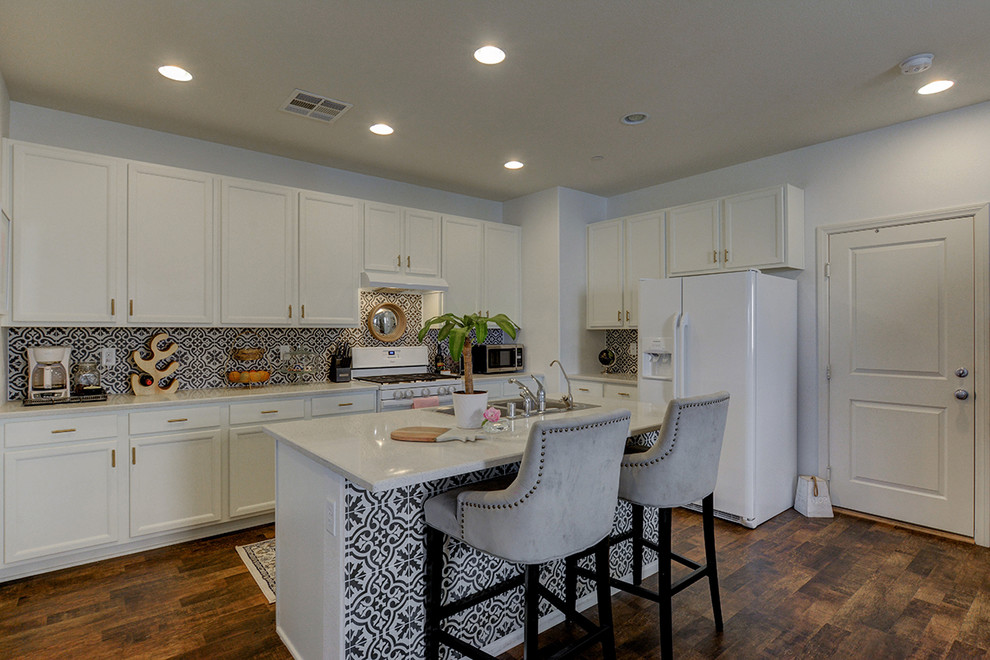Bild på ett mellanstort funkis linjärt kök och matrum, med en dubbel diskho, släta luckor, vita skåp, bänkskiva i kvartsit, grått stänkskydd, stänkskydd i terrakottakakel, vita vitvaror, laminatgolv, en köksö och brunt golv