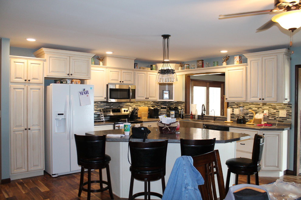 Photo of a large l-shaped enclosed kitchen in Other with a belfast sink, raised-panel cabinets, white cabinets, laminate countertops, stainless steel appliances and an island.