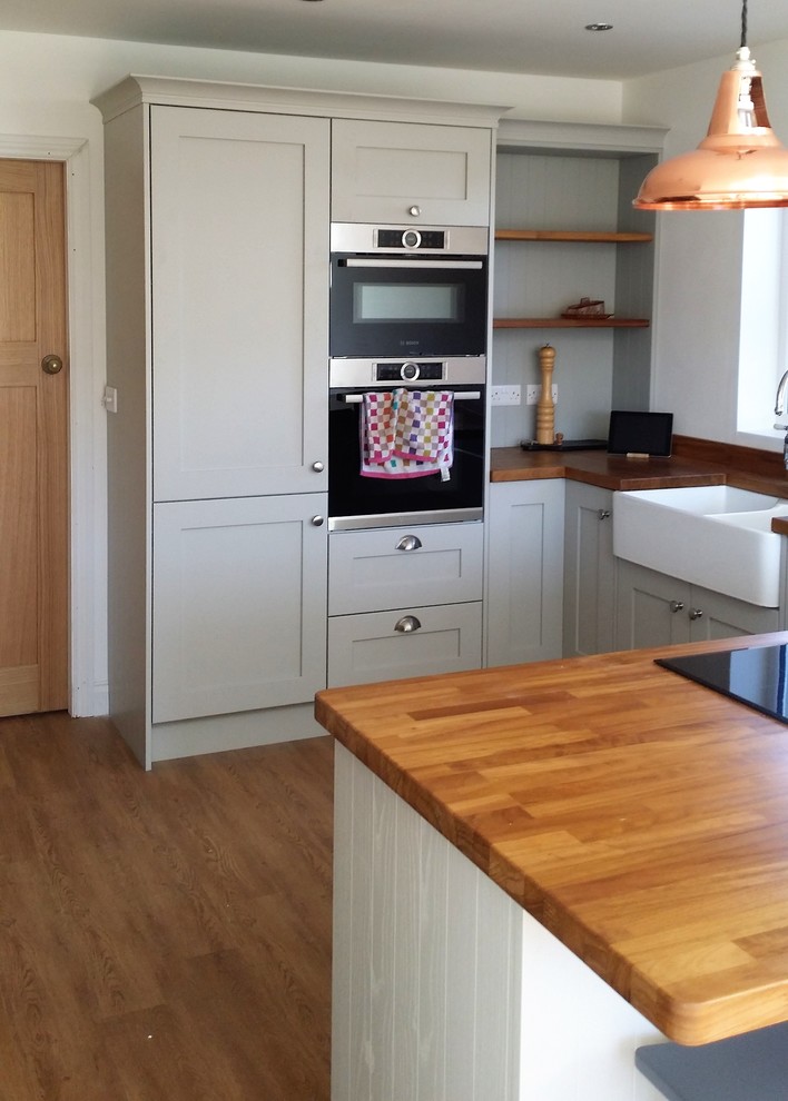 Photo of a medium sized farmhouse u-shaped open plan kitchen in Other with a belfast sink, shaker cabinets, grey cabinets, wood worktops, integrated appliances, medium hardwood flooring and a breakfast bar.