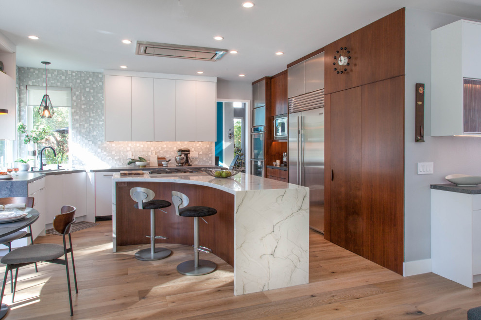 This is an example of a medium sized traditional u-shaped open plan kitchen in Denver with a submerged sink, flat-panel cabinets, white cabinets, quartz worktops, white splashback, glass tiled splashback, stainless steel appliances, medium hardwood flooring, an island, beige floors and white worktops.