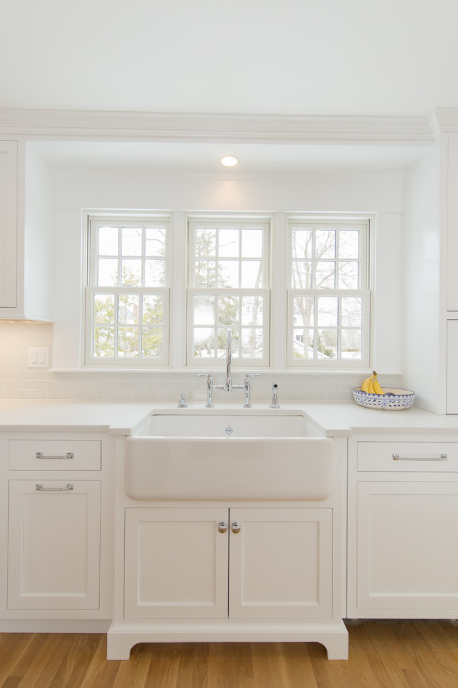 Klassisk inredning av ett mellanstort vit vitt kök, med en rustik diskho, skåp i shakerstil, vita skåp, bänkskiva i kvarts, vitt stänkskydd, stänkskydd i tunnelbanekakel, integrerade vitvaror, mellanmörkt trägolv, en köksö och brunt golv