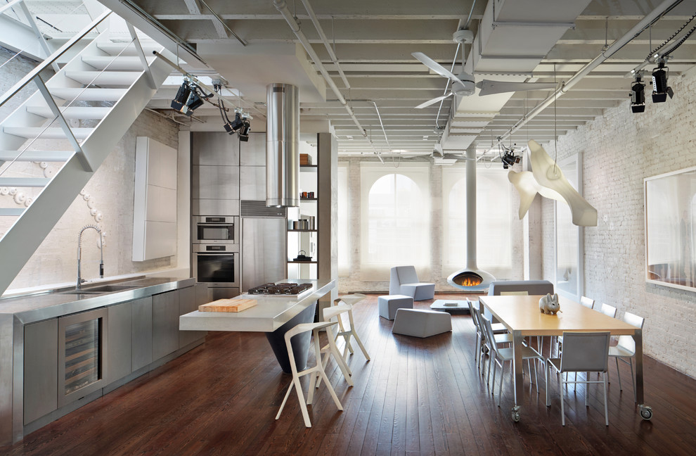 Foto på ett industriellt flerfärgad kök, med släta luckor, grå skåp, bänkskiva i rostfritt stål, en integrerad diskho, vitt stänkskydd, stänkskydd i tegel, rostfria vitvaror, mörkt trägolv och brunt golv