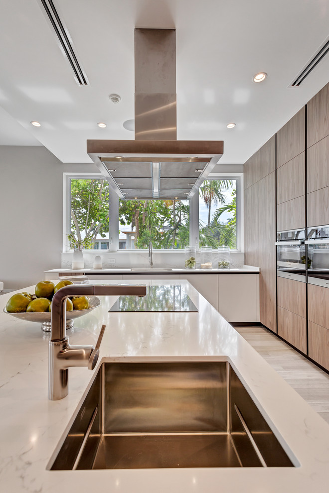 Moderne Küche in L-Form mit Waschbecken, flächenbündigen Schrankfronten, hellbraunen Holzschränken, Küchenrückwand in Weiß, Küchengeräten aus Edelstahl, hellem Holzboden, Kücheninsel, beigem Boden und weißer Arbeitsplatte in Miami