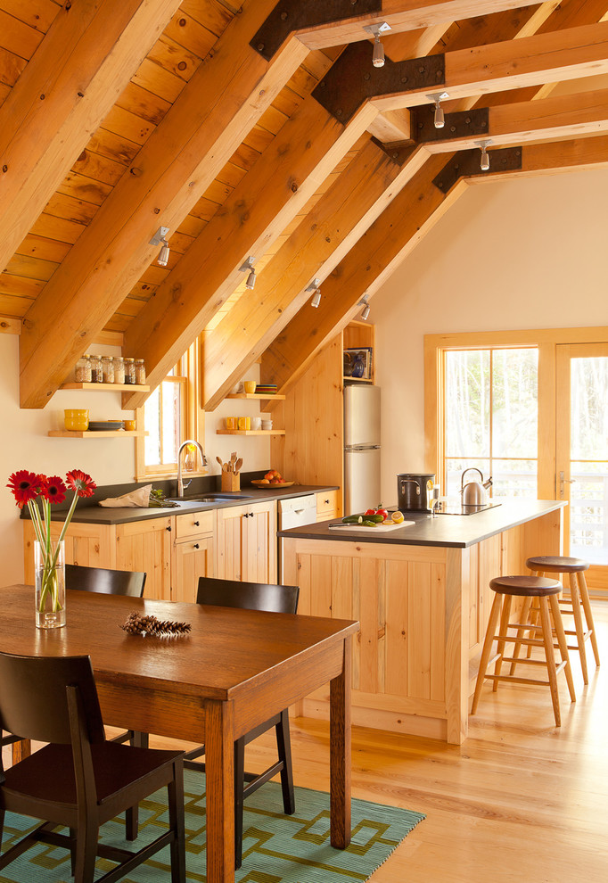 Example of a cottage single-wall medium tone wood floor and beige floor open concept kitchen design in Portland Maine with an undermount sink, beige cabinets, black backsplash, stainless steel appliances, an island and black countertops