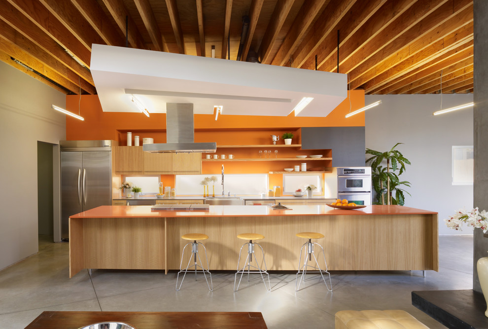 Zweizeilige Moderne Küche mit flächenbündigen Schrankfronten, hellen Holzschränken, Küchenrückwand in Orange, Küchengeräten aus Edelstahl, Betonboden, Kücheninsel, grauem Boden und oranger Arbeitsplatte in Los Angeles