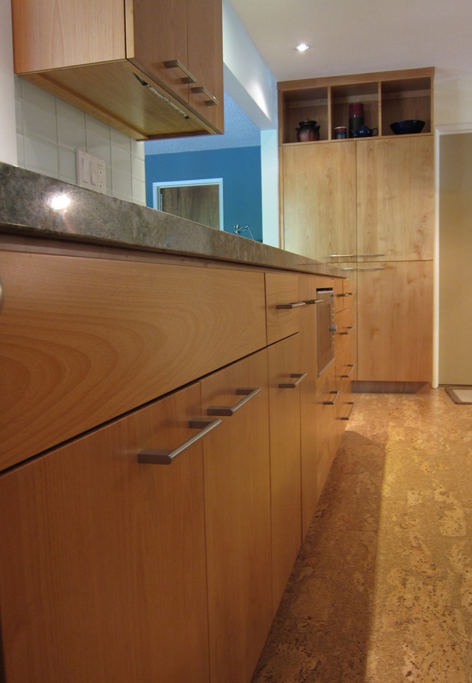 Modern u-shaped kitchen in San Francisco with stainless steel appliances, cork flooring, flat-panel cabinets, light wood cabinets, granite worktops, glass tiled splashback and grey splashback.