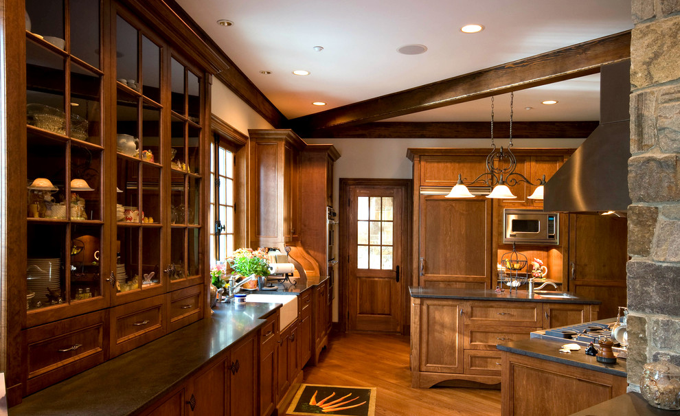 Modelo de cocina rústica con fregadero sobremueble, armarios con paneles empotrados, puertas de armario de madera oscura y electrodomésticos con paneles