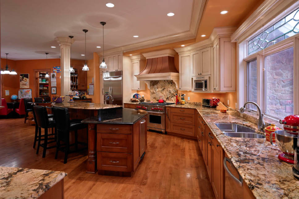 Große Klassische Küche in U-Form mit Schrankfronten mit vertiefter Füllung, hellen Holzschränken, Granit-Arbeitsplatte, Küchenrückwand in Orange, braunem Holzboden, zwei Kücheninseln und Doppelwaschbecken in Cleveland
