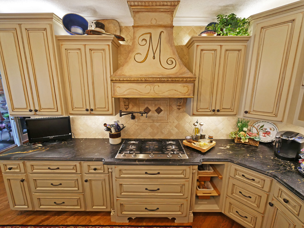 Eat-in kitchen - large traditional galley medium tone wood floor eat-in kitchen idea in Other with an integrated sink, raised-panel cabinets, distressed cabinets, granite countertops, beige backsplash, stone tile backsplash, paneled appliances and an island