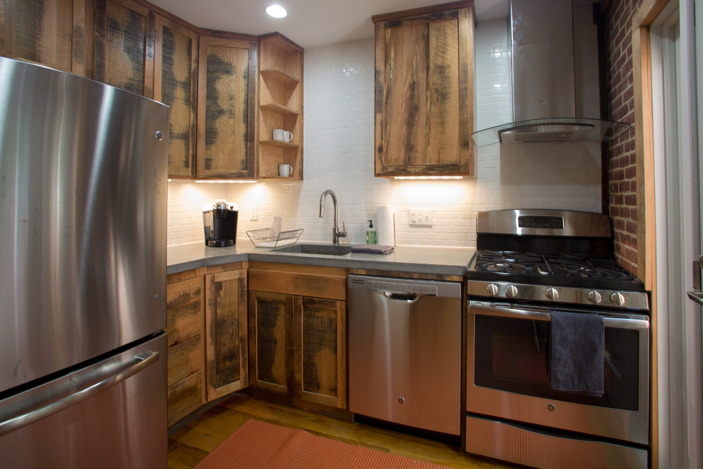 This is an example of a small modern l-shaped enclosed kitchen in Baltimore with a submerged sink, recessed-panel cabinets, distressed cabinets, concrete worktops, white splashback, ceramic splashback, stainless steel appliances, medium hardwood flooring, no island and brown floors.