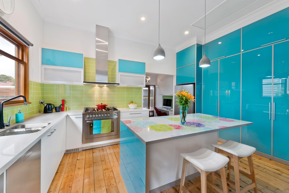Bild på ett avskilt funkis flerfärgad flerfärgat kök, med släta luckor, blå skåp, grönt stänkskydd, rostfria vitvaror, ljust trägolv och en köksö