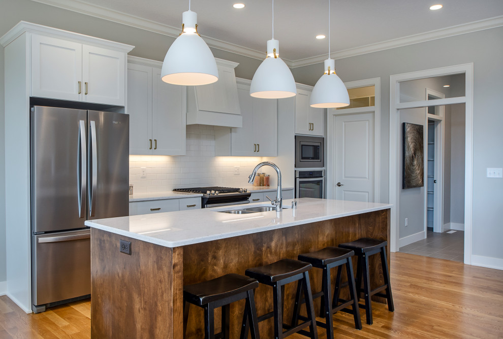 Mid-sized transitional galley medium tone wood floor and brown floor open concept kitchen photo in Other with a double-bowl sink, shaker cabinets, white cabinets, white backsplash, subway tile backsplash, stainless steel appliances, an island and white countertops