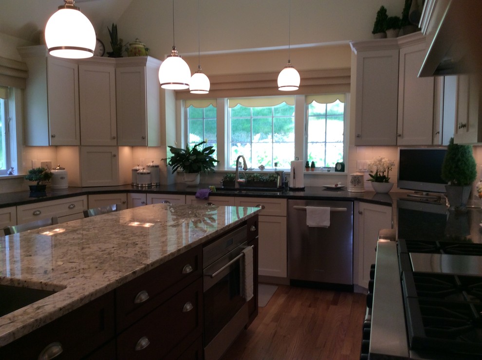 Example of a minimalist u-shaped medium tone wood floor kitchen design in New York with a drop-in sink, raised-panel cabinets, white cabinets, granite countertops, white backsplash, porcelain backsplash, stainless steel appliances, an island and black countertops
