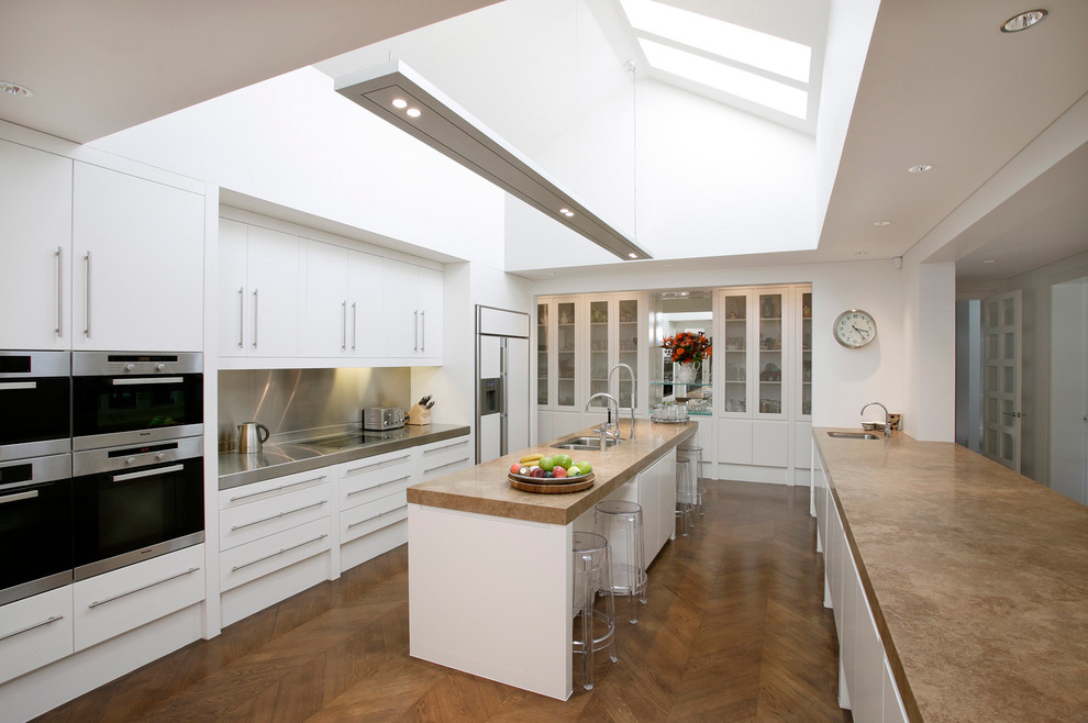 Moderne Küche in U-Form mit Unterbauwaschbecken, flächenbündigen Schrankfronten, weißen Schränken, Küchenrückwand in Metallic, braunem Holzboden und Kücheninsel in Sydney